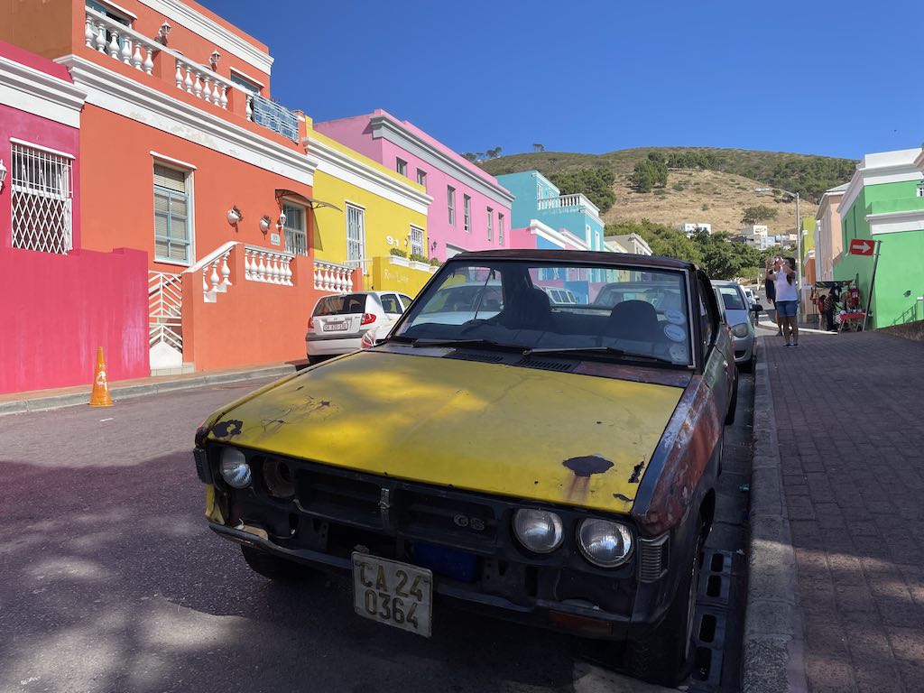 A vintage beaten up car parked outside the colourful houses of Bo Kaap In Cape Town